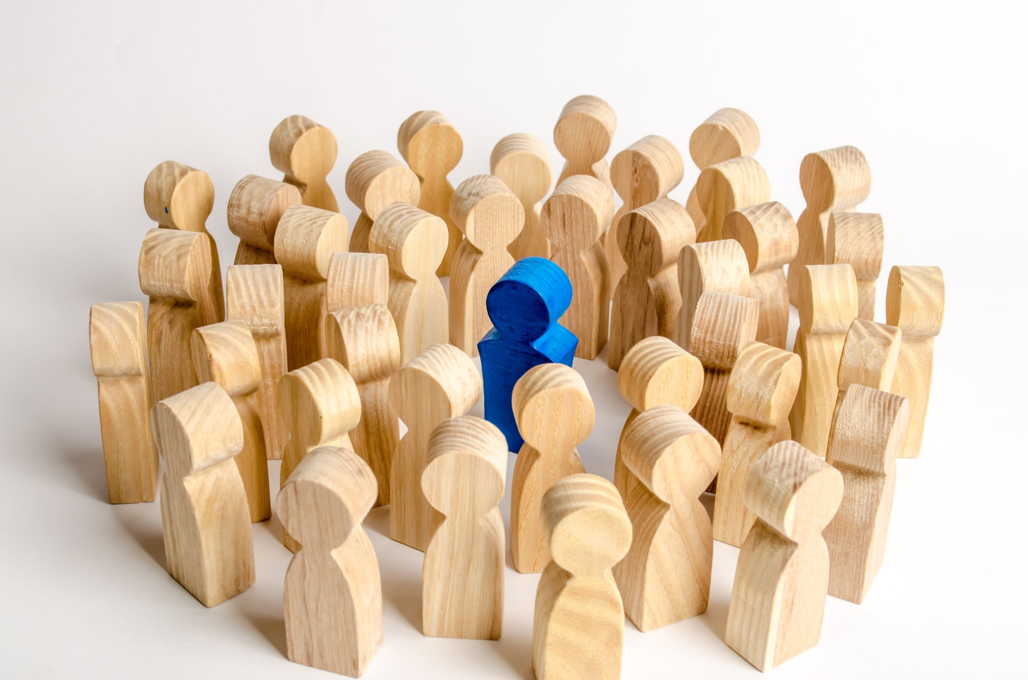 Un bonhomme en bois bleu entourés par de nombreux bonhommes en bois naturel qui le regardent